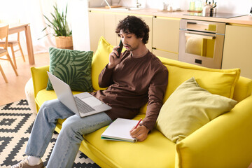 Young man engages in a phone conversation while working on a laptop at home