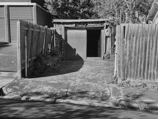 Black and white photograph of a disintegrating garage, only able to accommodate a tiny car, in disrepair at the rear of a property. Urban decay merges with creativity in this gritty street scene.