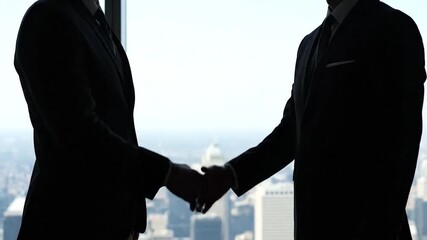 Silhouetted businessmen shake hands against a cityscape backdrop. A deal is sealed - Powered by Adobe
