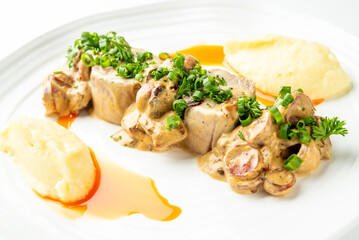 A beautifully plated dish featuring sliced pork or chicken with a creamy mushroom sauce and fresh herbs, served with two portions of mashed potatoes and a savory jus.