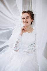 A smiling bride in a white lace wedding dress poses with her veil flowing gracefully around her. The soft fabric and natural light create a romantic and dreamy bridal portrait.