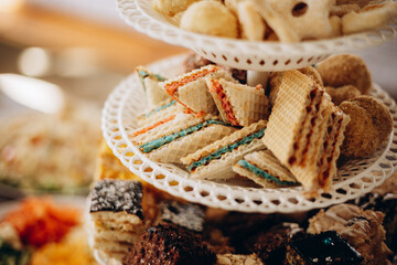 A three-tier dessert stand with wafer cakes filled with colorful cream layers and homemade pastries. The sweet assortment creates a cozy and festive atmosphere.
