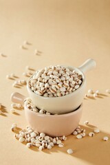 Raw Coix Seeds in Ceramic Cups on Beige Background