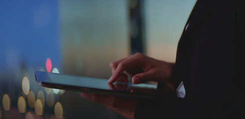 Business professional actively using a touch screen tablet checking digital data and connecting with technology at night with city lights creating a dynamic blurred background