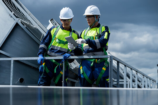 Two men in safety gear are looking at a tablet - Powered by Adobe