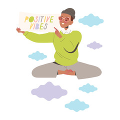 Smiling woman in light green sweater and gray pants meditating while holding a sign with colorful text 