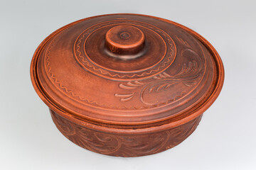 Round red clay roaster with closed lid on gray background