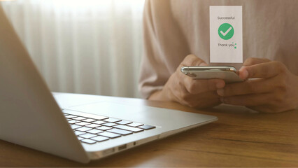 Online payment successful on smartphone with laptop on wooden desk, person expression in bright home office setting
