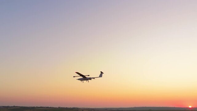 Aerial shot of fixed wing drone taking off above agricultural fields at sunrise