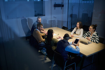 Diverse business team gathered around a table discussing analytics during a meeting in a modern office. Laptop screen shows charts and graphs, symbolizing teamwork, communication, and data driven