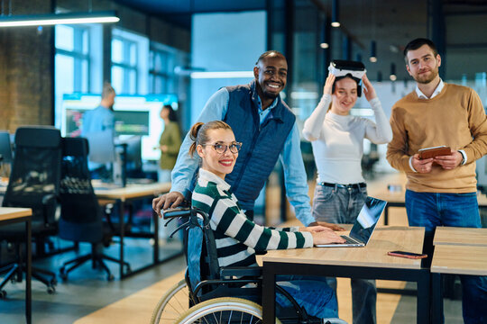 Diverse business team collaborating in a modern office environment. A woman in a wheelchair works on a laptop while colleagues explore virtual reality and digital tools, promoting innovation