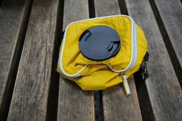 Yellow camera bag with lens cap on wooden bench