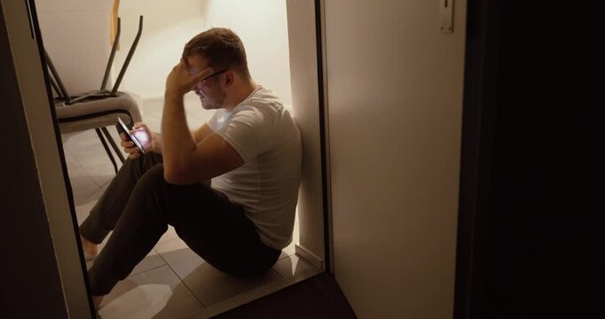 A man sits on the floor, visibly frustrated by what he sees on his smartphone. Perfect for themes like social media stress, dating apps, AI, deepfakes, online jobs, or digital burnout.