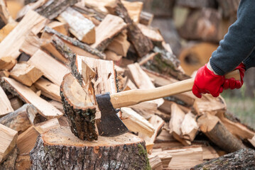 A man splitting a log with an axe against a background of firewood. The moment of wood splitting: an axe strikes a log on a stump, hard physical labor, strength, preparation for winter