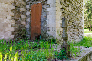 Rustic stone building with weathered wooden door and overgrown wild grass