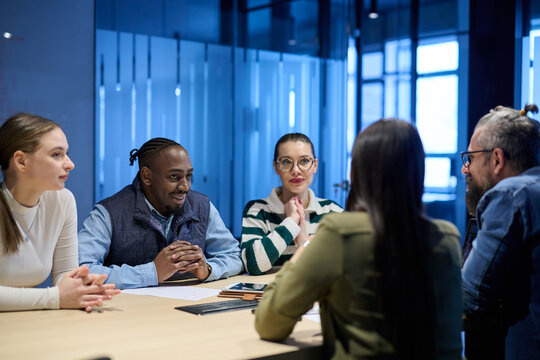 Diverse business team gathered around a table discussing analytics during a meeting in a modern office. Laptop screen shows charts and graphs, symbolizing teamwork, communication, and data driven
