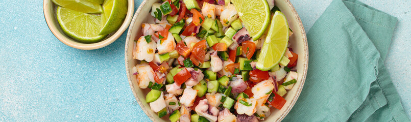 Fresh and vibrant peruvian seafood ceviche with shrimps, octopus, tomatoes, cucumber and parsley, served with lime in a bowl on a light blue background from above, dish of Peru