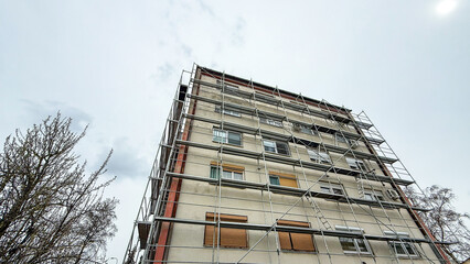 Under a somber sky, industrial scaffolding cradles an urban monolith, echoing Festivus for ironworkers, renewal whispers