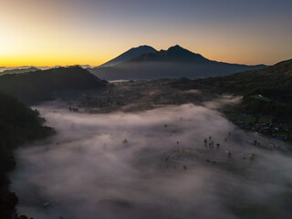 Aerial drone view of misty  Kintamani valley at mount Batur, Bali sunrise with mountains in the background, creating a dramatic and serene natural landscape.