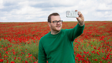 A Caucasian man joyfully captures a selfie amidst vibrant poppy fields, evoking Poppy Day...