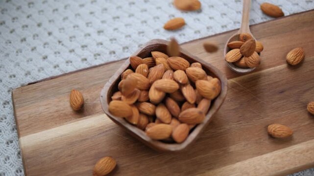 Roasted whole almonds slowly falling from above into a rustic wooden bowl on a cutting board, representing a healthy lifestyle, superfood nutrition, and organic vegetarian snacking