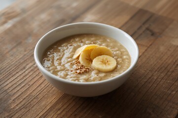 Light breakfast bowl of millet and banana porridge on a wooden surface