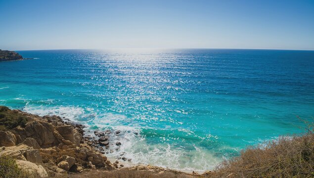 Sandy shoreline with rocky cliffs and a vast blue sea under a clear sky - Powered by Adobe