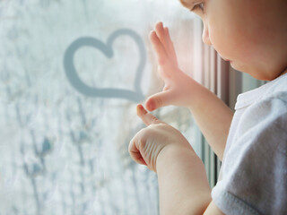 A little boy draws a heart on a winter window.