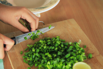 hands cutting green spring onion on cutting board for cooking