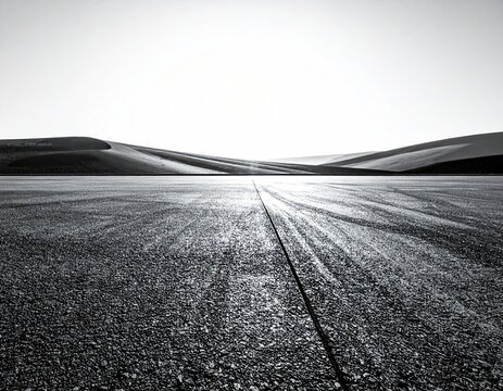A black and white photo with a straight, paved road leading to rolling desert hills under a bright sky - Powered by Adobe