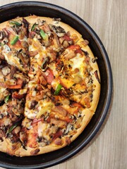Delicious Super Supreme pizza with toppings of smoked beef, beef burger, smoked chicken, mozzarella cheese, mushrooms, pineapple, red peppers and green peppers put on a wooden table and ready to eat