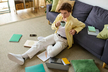 Young man enjoys coffee while working in a cozy living room on a sunny afternoon