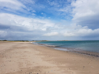 Sandy seaside beach in Castlegregory, Dingle Peninsula, County Kerry, Ireland. Cloudy blue sky with mountains hills in the distance.