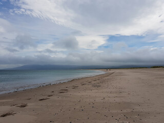 Footprints in the sand seaside beach in Castlegregory, Dingle Peninsula, County Kerry, Ireland. Cloudy blue sky with mountains hills in the distance.