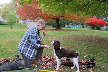 Middle-aged man takes a break from raking leaves to pet his dog
