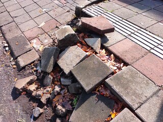 Broken paving stones and debris on a damaged sidewalk on Ijen street, Malang, Indonesia.