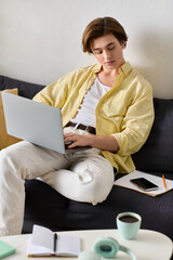 Fototapeta premium Young man working on laptop while relaxing at home with coffee and notes around him