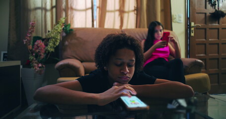 Boy engrossed in smartphone at glass table, girl behind on sofa immersed in phone, illustrating...