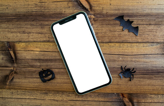 Mockup, smartphone, paper black bat, spider and pumpkin on wooden background. Halloween background.