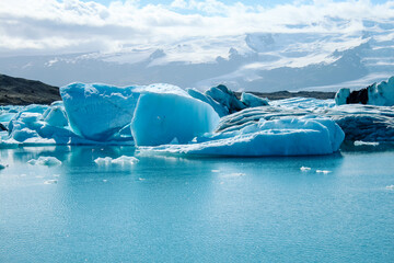 Panoramic view of floating icebergs scattered across Jökulsárlón glacier lagoon, Iceland. The image showcases the contrast between icy blue tones, dark volcanic sand, and glacial reflections.