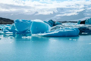 Fototapeten Gletscher Panoramic view of floating icebergs scattered across Jökulsárlón glacier lagoon, Iceland. The image showcases the contrast between icy blue tones, dark volcanic sand, and glacial reflections.  © Gloria
