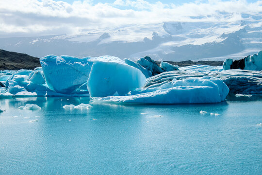Panoramic view of floating icebergs scattered across Jökulsárlón glacier lagoon, Iceland. The image showcases the contrast between icy blue tones, dark volcanic sand, and glacial reflections. - Powered by Adobe