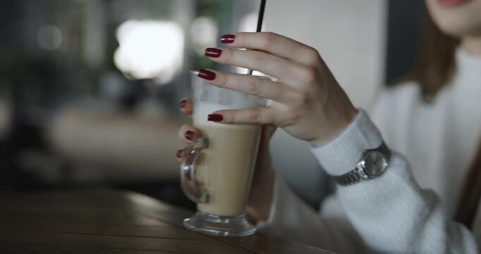 Woman hand take a glass with latte in cafe and drinking it