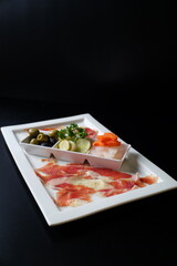 A gourmet platter with an array of delicious appetizers, beautifully arranged, offering a tempting culinary experience. The platter features cured meat, fresh vegetables, and olives.