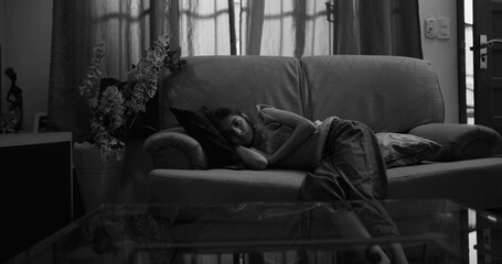 Monochromatic portrait of a young girl lying on a couch, gazing blankly with a somber expression, embodying themes of isolation, melancholy, and emotional stillness in a serene, muted setting © Marco