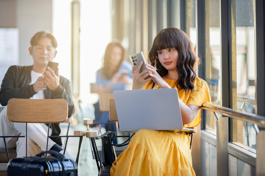 Group of Multi ethnic people are sitting near window at the departure area of the airport, enjoying using devices, smartphone, laptop. Trendy technology concept 