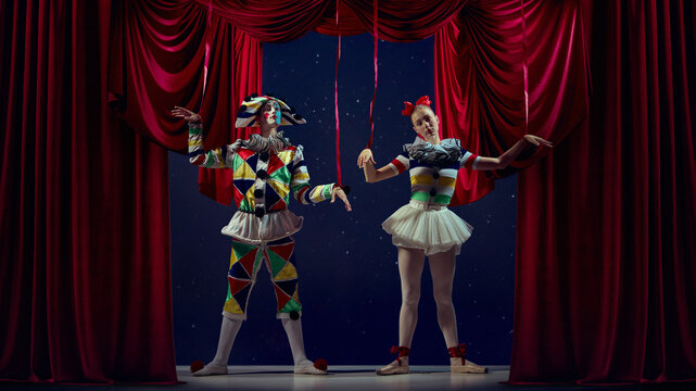 Puppets of stage. Mime and ballerina posing as marionettes under red curtains. Concept of control, duality, identity used in editorial, metaphorical, and theater storytelling.