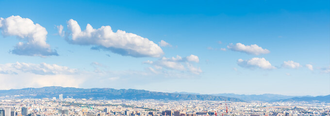Wide panoramic Osaka Japan cityscape view of a large city with a mountain range in the background. Beautiful clear blue sky with white clouds.