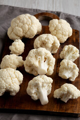 White Organic Raw Cauliflower Florets on a Wooden Board, side view.
