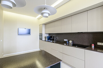 Modern kitchen with sleek cabinets, dark countertops, and unique lighting fixtures. A clean, minimalist design